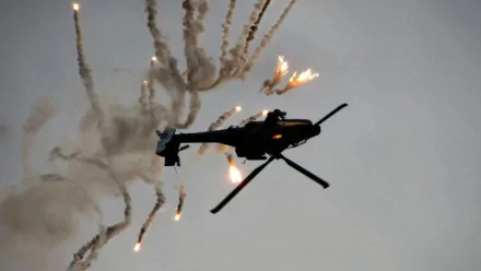 HD desktop wallpaper showcasing a Boeing AH-64 Apache military helicopter deploying flares against a grey sky.
