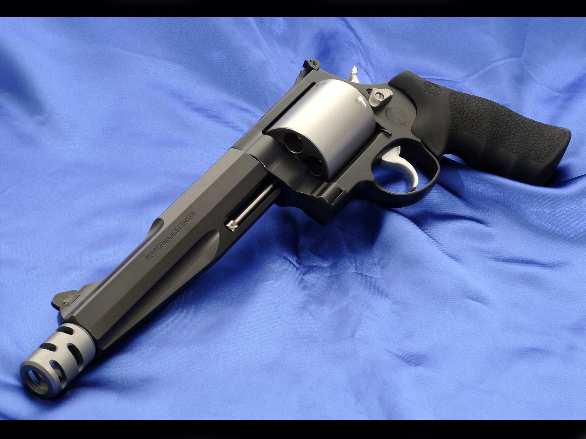High-definition desktop wallpaper featuring a Smith & Wesson revolver with a black grip resting on a blue fabric background.