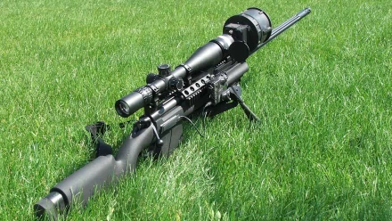 A close-up of a sniper rifle resting on vibrant green grass, showcasing the intricate details of its design. This HD image serves as a striking desktop wallpaper and background.