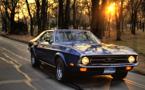 HD desktop wallpaper featuring a classic Ford Mustang driving on a road with trees and a beautiful sunset in the background.