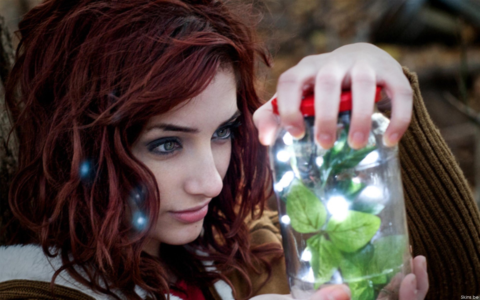 A captivating HD wallpaper featuring Susan Coffey, showcasing her holding a jar with glowing lights and green leaves, set against a natural backdrop.