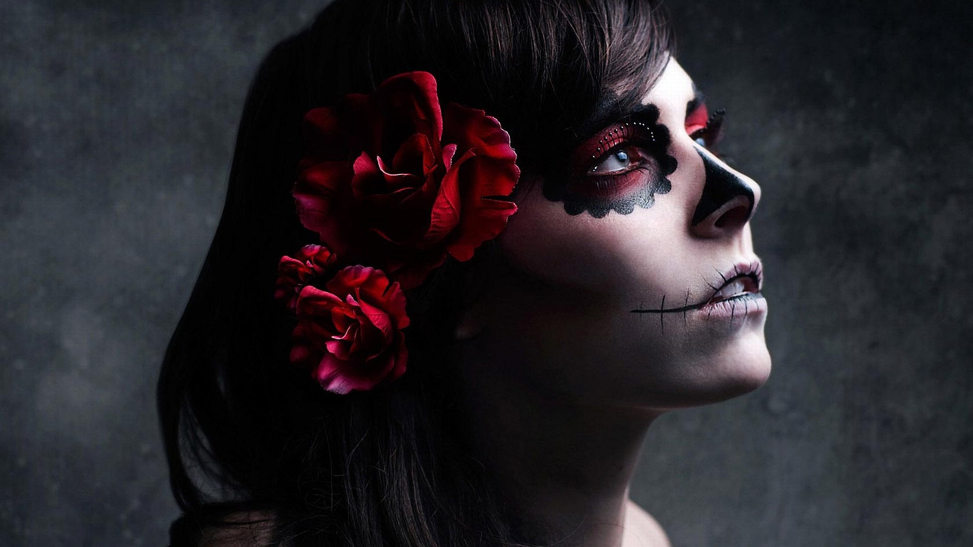 HD fantasy desktop wallpaper featuring a woman with dark hair, red roses, and intricate skull face paint against a smoky, textured background.
