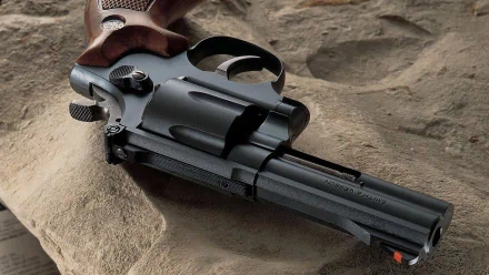 HD desktop wallpaper featuring a close-up of a man-made Smith & Wesson revolver resting on a textured stone surface.