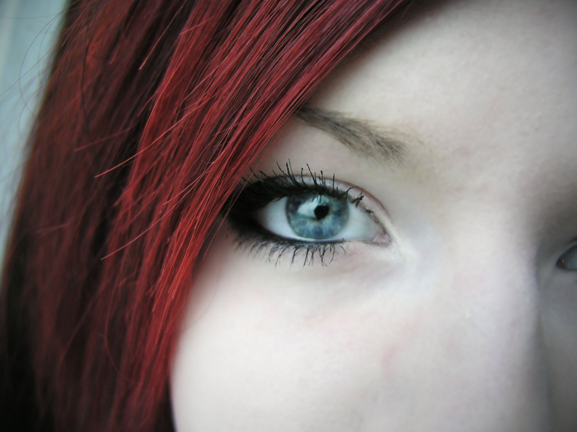 Close-up of a woman's face highlighting striking blue eyes and vibrant red hair, designed as high-definition wallpaper and background.