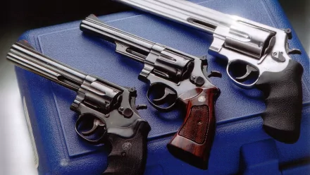 HD desktop wallpaper featuring three man-made revolvers with varied finishes and wooden grips arranged on a textured blue surface.