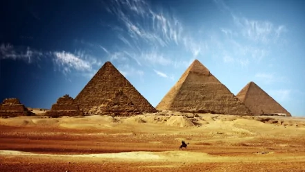 A stunning HD desktop wallpaper featuring a row of majestic pyramids under a vast blue sky, with a lone figure riding in the foreground across the sandy landscape.
