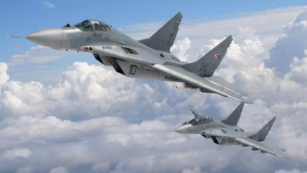 Two Mikoyan MiG-29 fighter jets soar through a clear blue sky, surrounded by fluffy white clouds. This high-definition image captures the essence of military aviation.