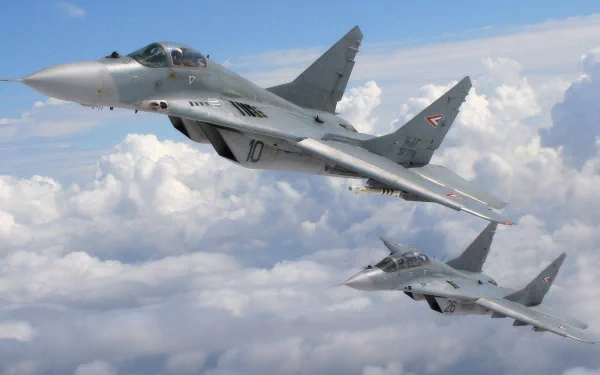 Two Mikoyan MiG-29 fighter jets soar through a clear blue sky, surrounded by fluffy white clouds. This high-definition image captures the essence of military aviation.