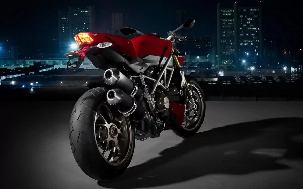 Red Ducati motorcycle parked on a rooftop at night against an illuminated city skyline — HD PC desktop wallpaper/background.