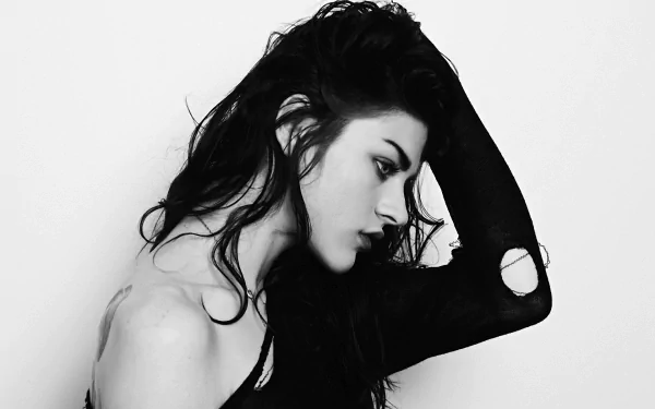 Black and white HD wallpaper featuring a woman, tagged as Frances Bean Cobain, striking a contemplative pose with her hand in her hair, set against a plain background.