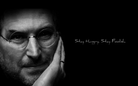 Black and white HD wallpaper featuring Steve Jobs against a dark background with the quote Stay Hungry. Stay Foolish written in white text.