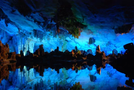 HD PC desktop wallpaper showcasing the stunning natural beauty of Reed Flute Cave with vibrant blue lighting highlighting limestone formations and their reflections in water.