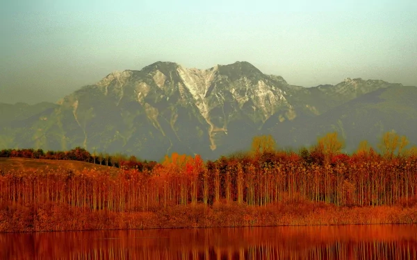 A tranquil scene featuring majestic mountains in the background, with vibrant autumnal trees reflecting in a calm body of water, suitable as a 4K Ultra HD PC desktop wallpaper.