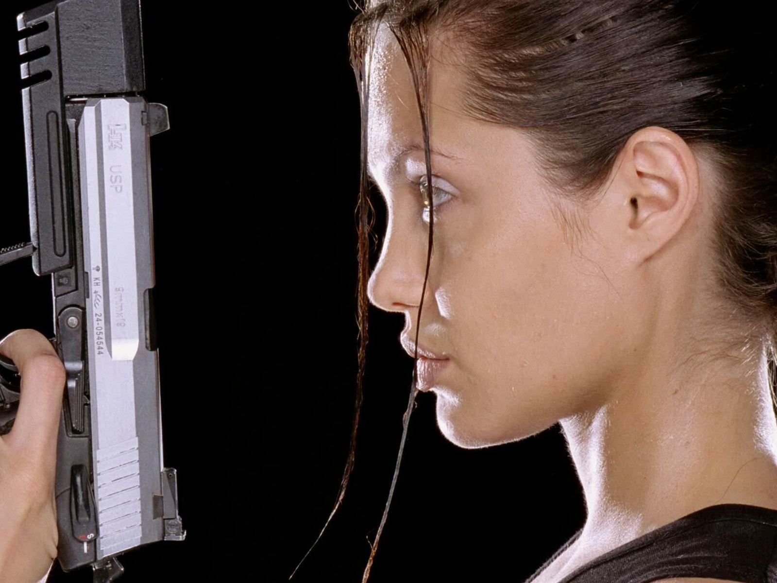HD desktop wallpaper featuring a close-up side profile of Angelina Jolie holding a gun, set against a black background.