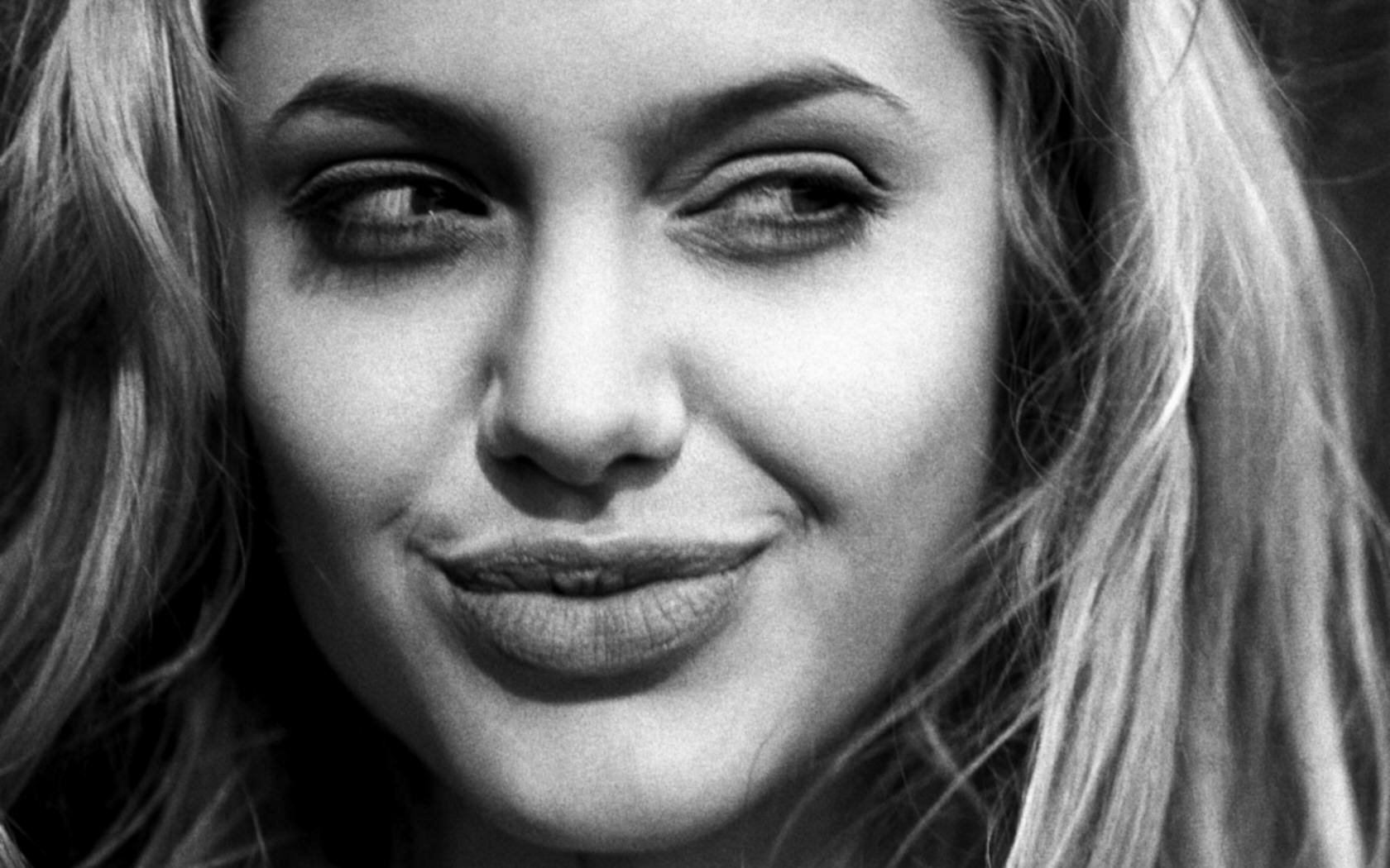 Black and white HD wallpaper featuring a close-up of Angelina Jolie, showcasing her expressive smile and captivating gaze. A striking background choice for fans.