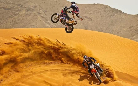 HD PC desktop wallpaper: motocross vehicles, two motorcycles racing over golden desert dunes, one rider airborne with sand trailing.