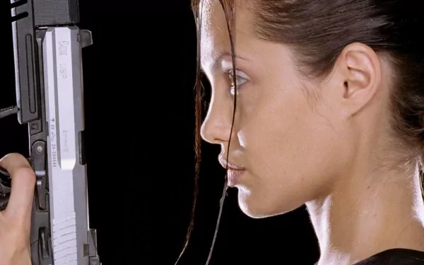 HD desktop wallpaper featuring a close-up side profile of Angelina Jolie holding a gun, set against a black background.
