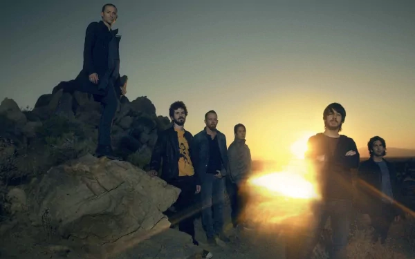 HD wallpaper featuring the band Linkin Park standing on rocks against a vibrant sunset backdrop, capturing a moment of musical artistry and energy.
