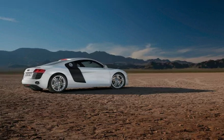 HD desktop wallpaper featuring a white Audi R8 sports car parked on a cracked desert landscape with mountains under a clear blue sky.