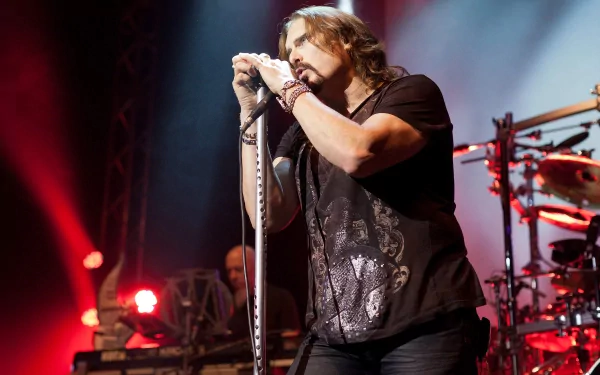 HD PC desktop wallpaper/background: live concert shot of a vocalist performing with Dream Theater under red and blue stage lights, gripping a microphone with drums lit behind him.
