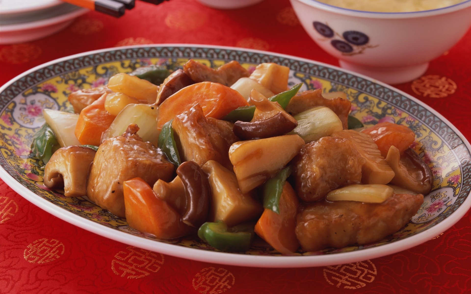 HD PC desktop wallpaper featuring a colorful plate of Chinese food with stir-fried vegetables and meat on a decorative dish against a red tablecloth background.