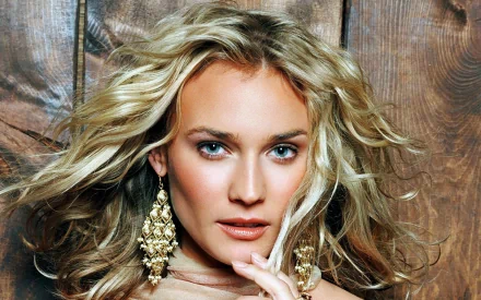 HD desktop wallpaper featuring celebrity Diane Kruger with flowing blonde hair and statement earrings against a rustic wooden background.