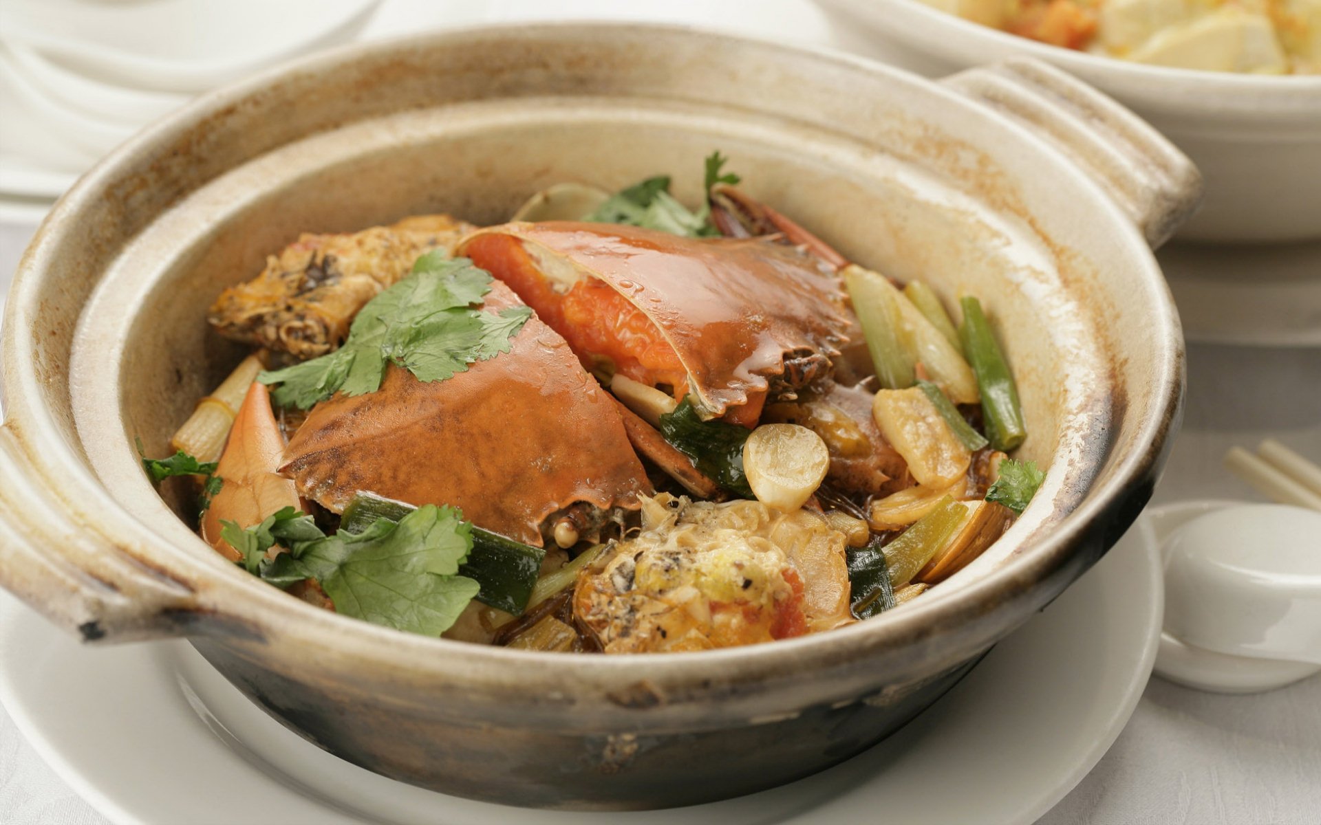 HD desktop wallpaper featuring a clay pot of Chinese food with crab, herbs, and vegetables in a savory sauce.