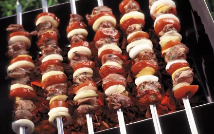 HD desktop wallpaper showing skewers of barbecue with grilled meat, onions, and tomatoes cooking over hot coals.