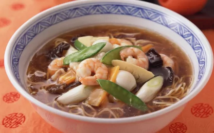 A vibrant bowl of Chinese shrimp noodle soup, featuring fresh vegetables and a rich broth, set against a decorative orange background. An appealing HD PC desktop wallpaper.