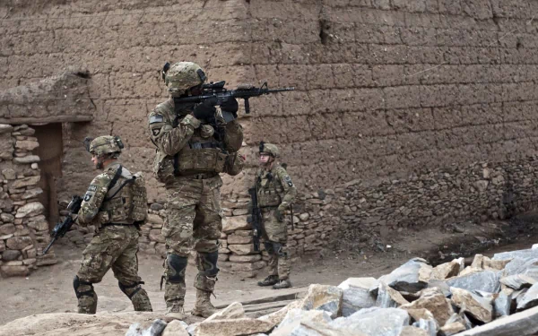 U.S. Army Infantry soldiers in full combat gear patrol a rugged war zone with mud-brick walls, captured in an HD military desktop wallpaper background.