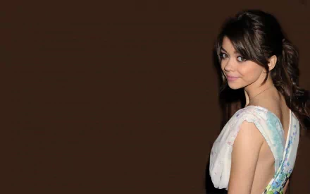 HD desktop wallpaper featuring celebrity Sarah Hyland posing against a dark brown background, showcasing her profile and elegant dress.