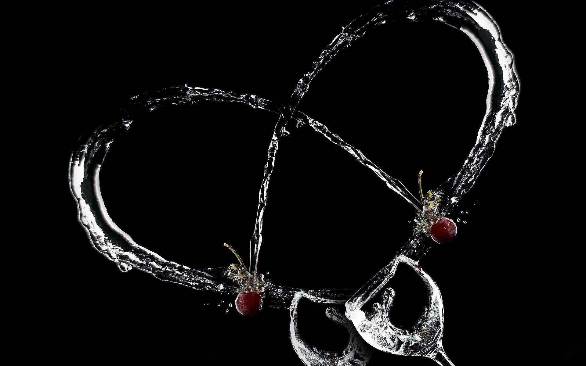 An artistic representation of love, featuring water splashes forming a heart shape around wine glasses, accented by raspberries, set against a dark background for a striking HD wallpaper.