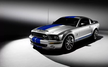 HD desktop wallpaper of a sleek silver Ford Mustang Shelby GT500 with blue racing stripes, showcased in a dramatic light and shadow setting.