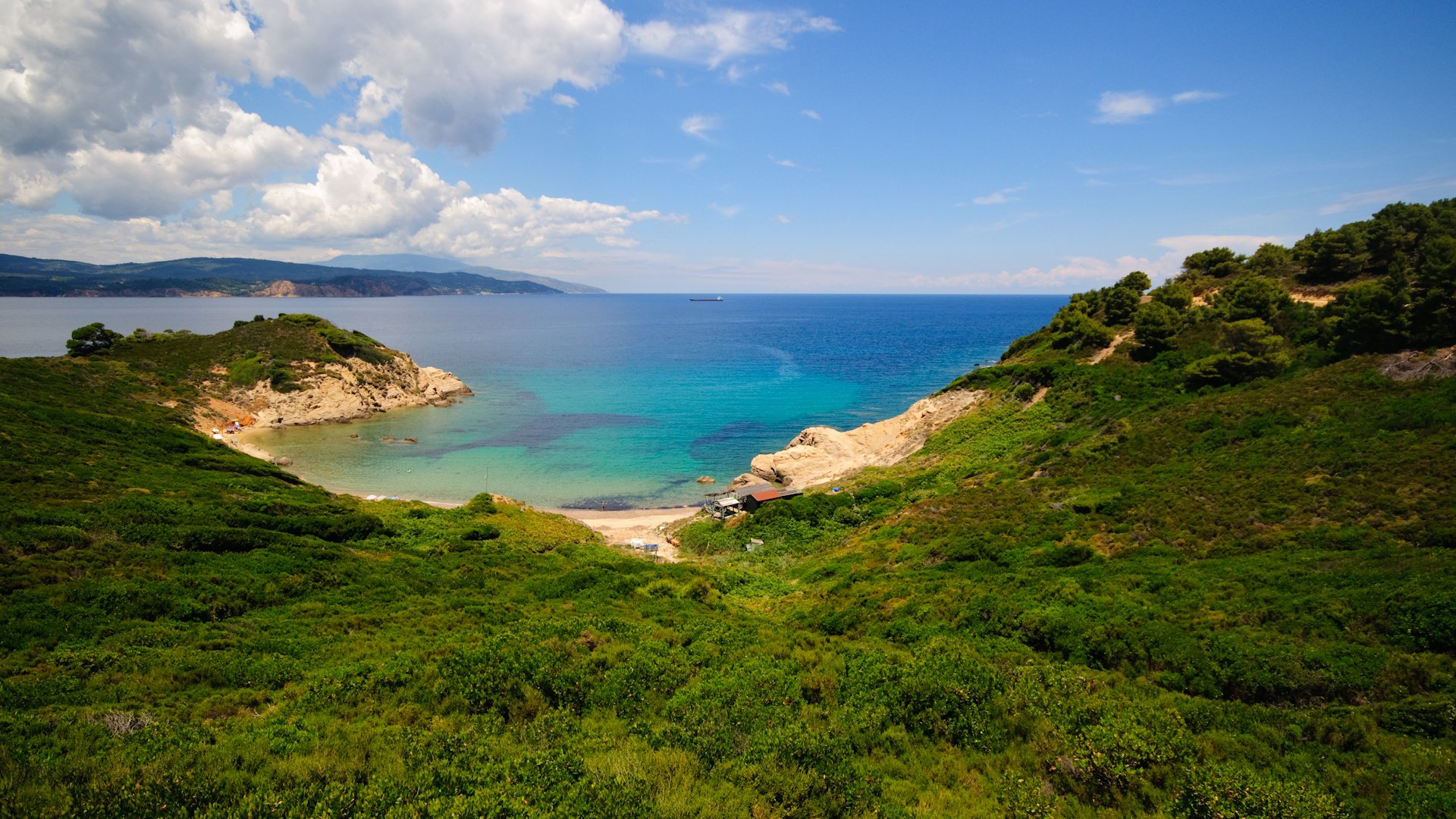 A serene seascape featuring lush green hills meeting a tranquil ocean under a partly cloudy sky, showcasing the beauty of nature in vibrant HD detail.