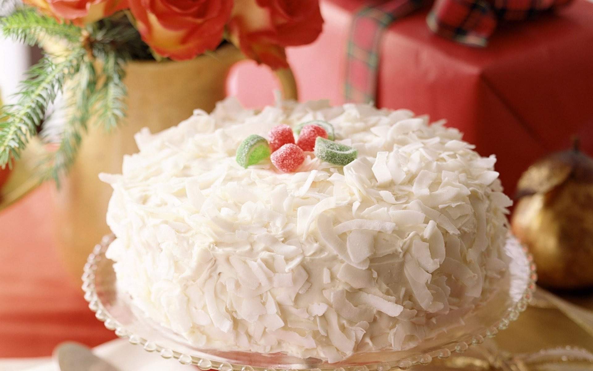 HD PC desktop wallpaper featuring a white cake decorated with coconut flakes and small red and green candies, set against a festive background with roses and wrapped gifts.