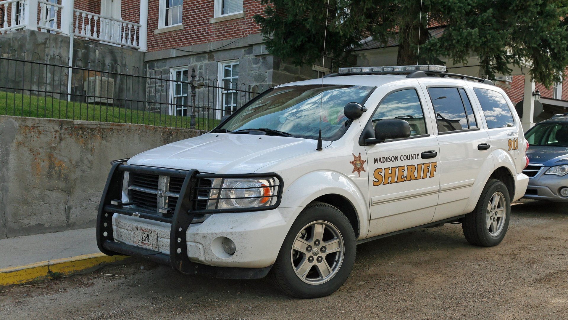 HD PC desktop wallpaper showing a white sheriff police vehicle (SUV) parked at a curb in front of a brick building.
