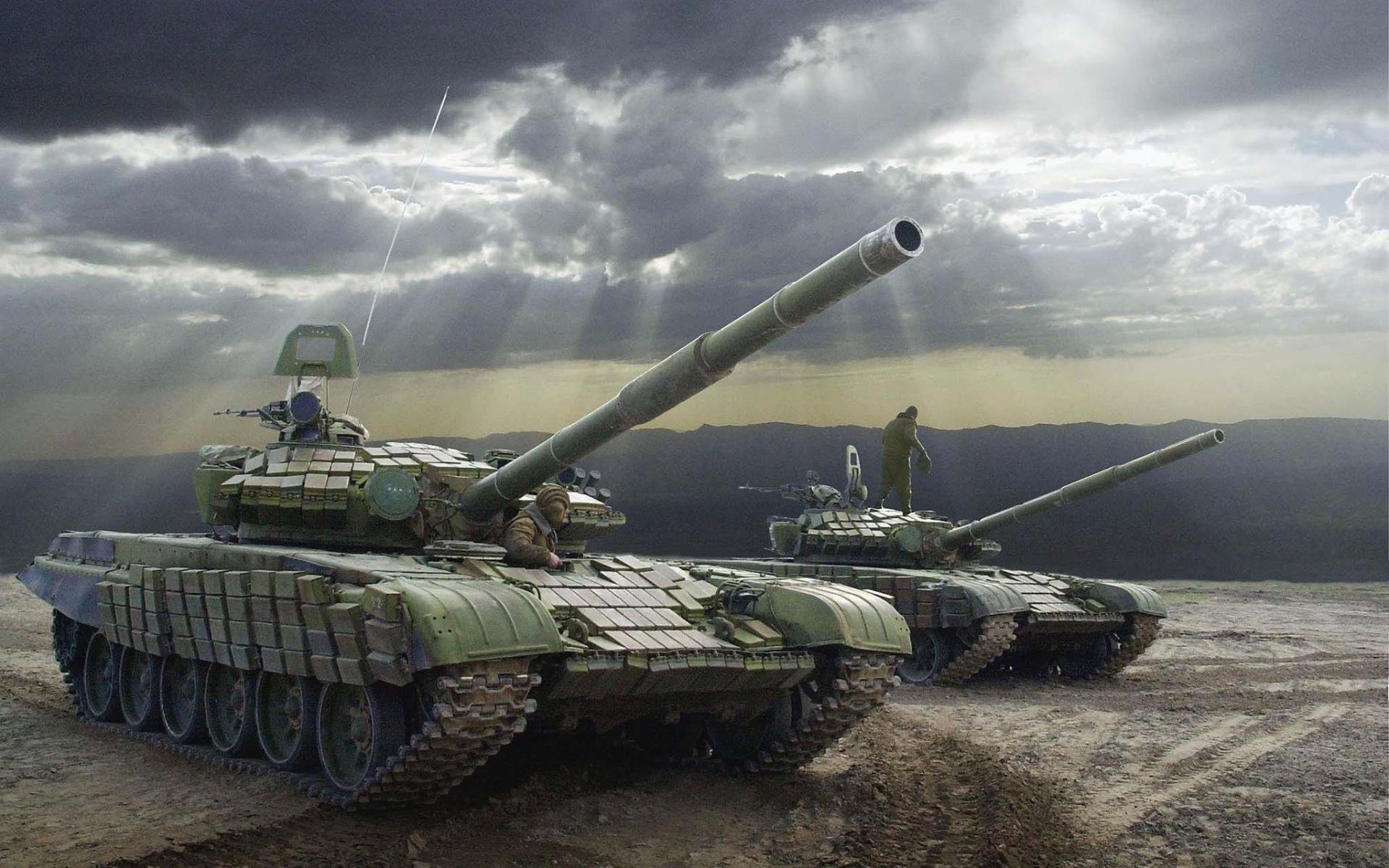 HD PC desktop wallpaper/background showing military tanks on barren terrain beneath a dramatic cloudy sky, two main battle tanks poised as sunbeams break through the clouds