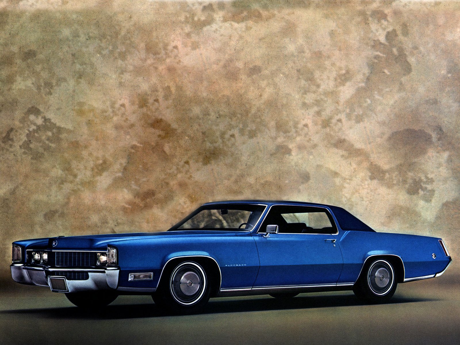 HD desktop wallpaper featuring a classic blue Cadillac vehicle against a textured beige background.