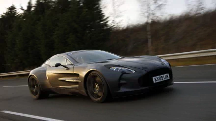 HD desktop wallpaper featuring a sleek black Aston Martin One-77 speeding on a forest-lined road.