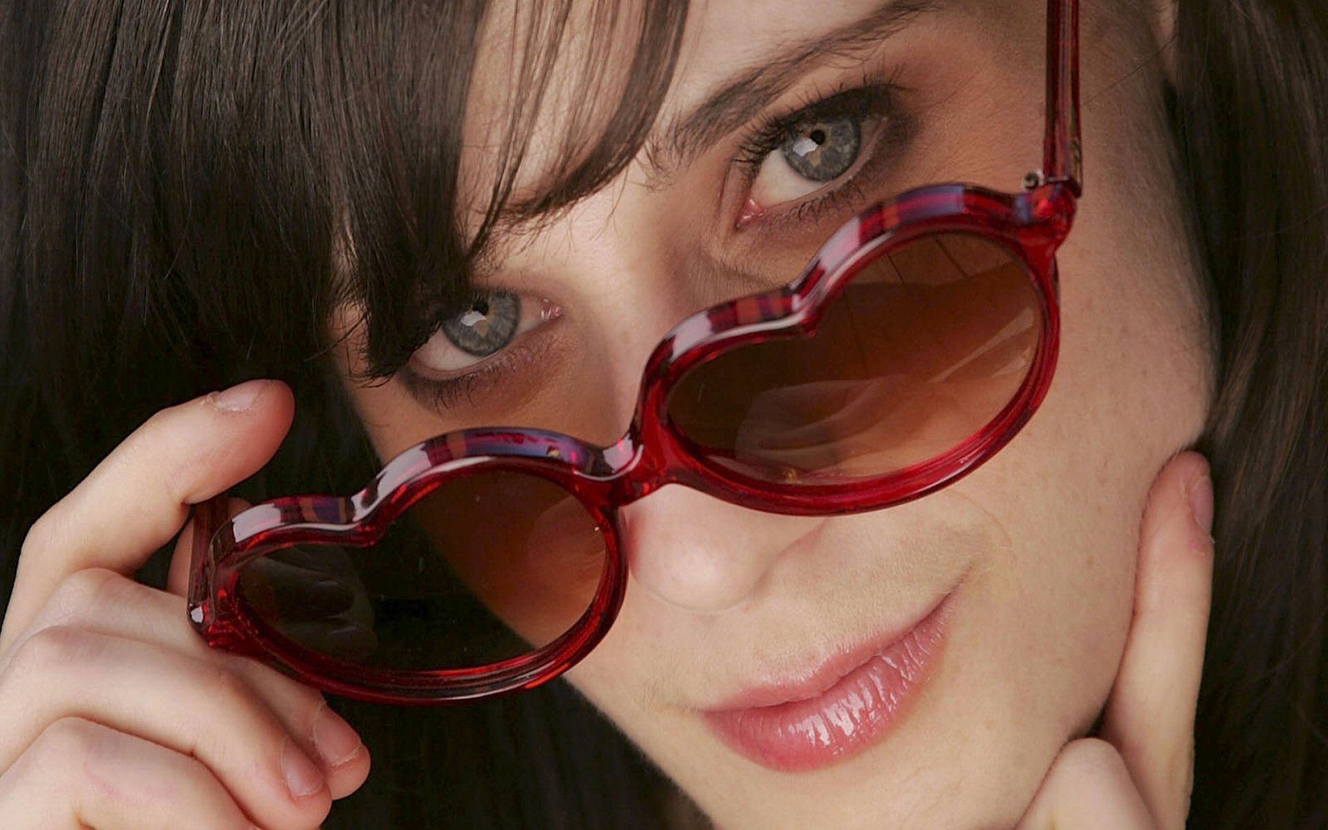 Close-up HD desktop wallpaper of celebrity Zooey Deschanel wearing heart-shaped red sunglasses, highlighting her expressive eyes and soft smile.