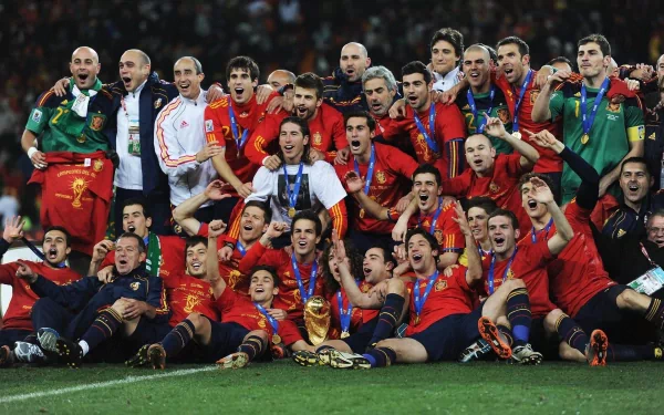HD PC desktop wallpaper of the Spain national football team celebrating with the trophy on the pitch — sports image of jubilant players and staff in red kits cheering together.