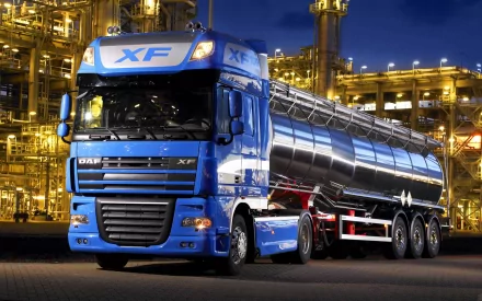 A striking HD wallpaper featuring a blue truck parked against an industrial backdrop, showcasing its sleek design and imposing presence in a nighttime setting.