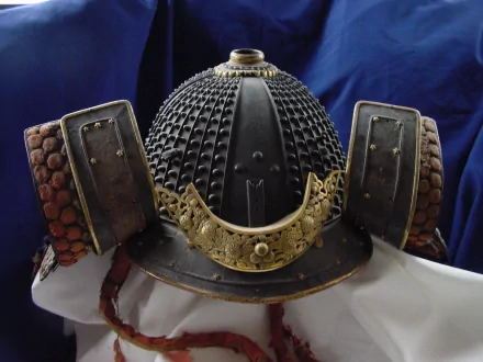 HD PC desktop wallpaper of a man-made ornate samurai helmet (kabuto) with a textured dome, gold crest and side guards set against a deep blue draped background.