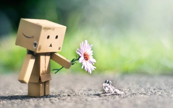 HD desktop wallpaper featuring a manipulated photograph of a small cardboard figure offering a flower to a tiny frog on a blurred natural background.