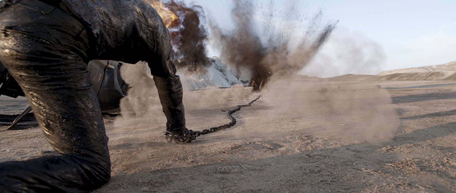 HD PC desktop wallpaper from the movie Ghost Rider: Spirit of Vengeance: a chain-wielding rider kneels on a desert floor as explosions blast dust and debris into the air.