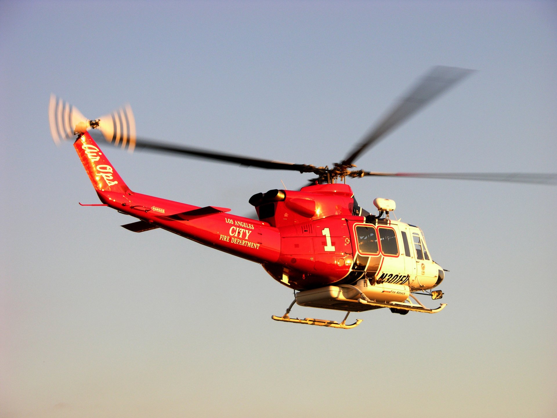 A red Bell 412 helicopter in flight against a clear sky, captured as an HD PC desktop wallpaper and background.
