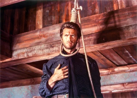 Clint Eastwood in a dramatic scene from The Good, the Bad and the Ugly, depicted as he confronts danger, framed against a rustic wooden backdrop. HD wallpaper for fans of classic cinema.