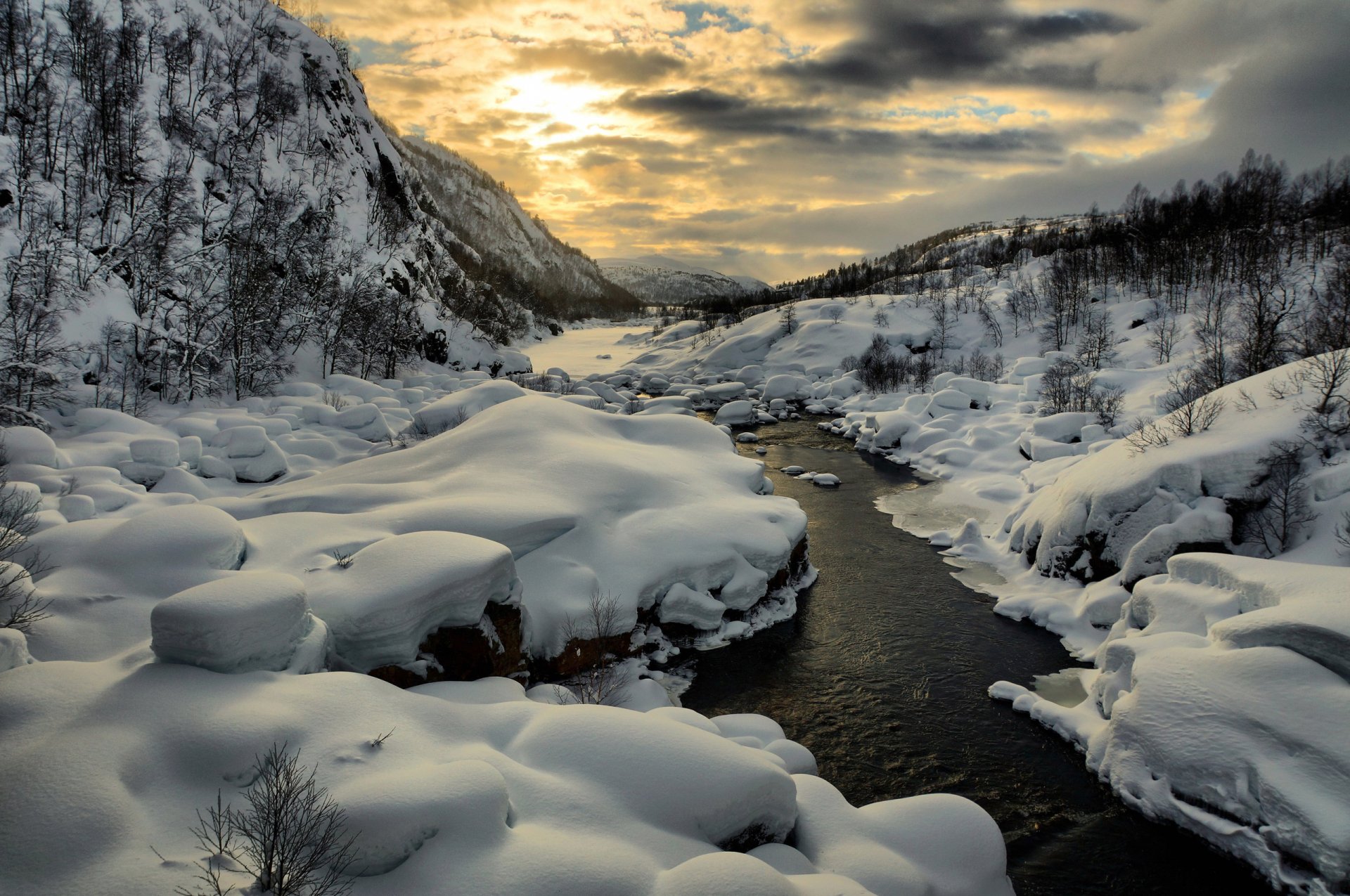Winter scene of a snow-covered mountain landscape with a flowing river and stream under a cloudy sky, captured in HD for a PC desktop wallpaper background.