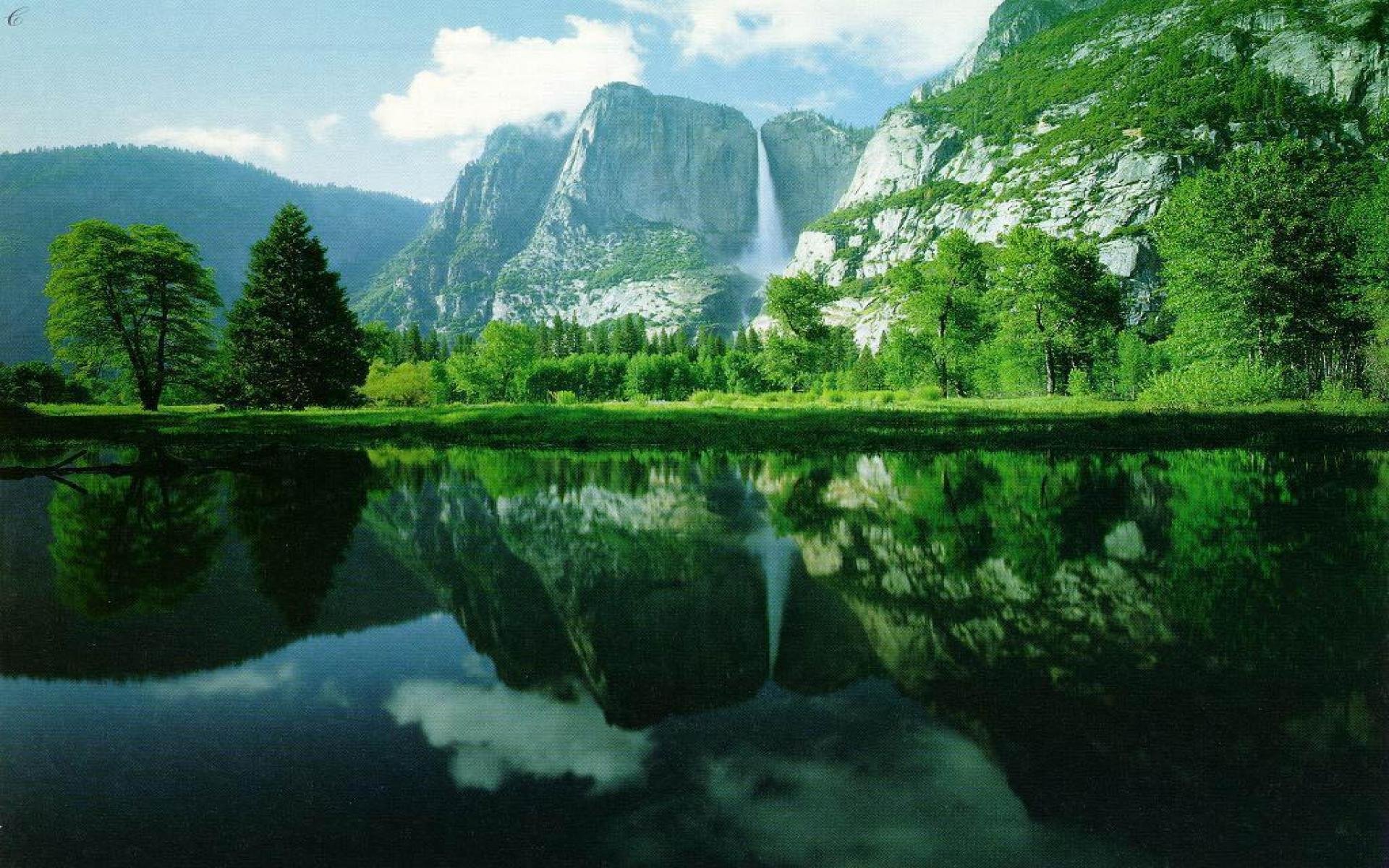 HD artistic desktop wallpaper showcasing a serene mountain landscape reflected in a calm lake, surrounded by lush greenery under a bright sky.