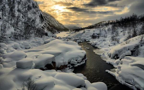 Winter scene of a snow-covered mountain landscape with a flowing river and stream under a cloudy sky, captured in HD for a PC desktop wallpaper background.